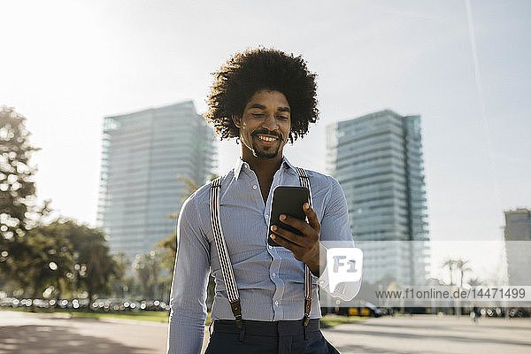 Spanien  Barcelona  Porträt eines lächelnden Mannes  der auf sein Handy schaut