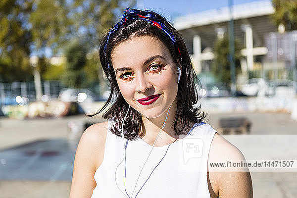Portrait of smiling young woman with earbuds in the city