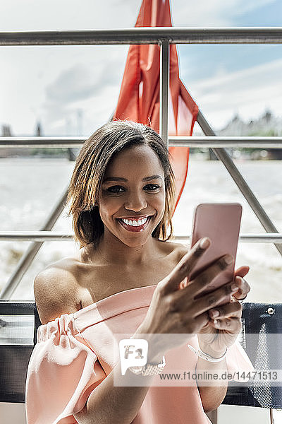 UK  London  portrait of beautiful smiling woman holding cell phone while traveling by boat on the River Thames