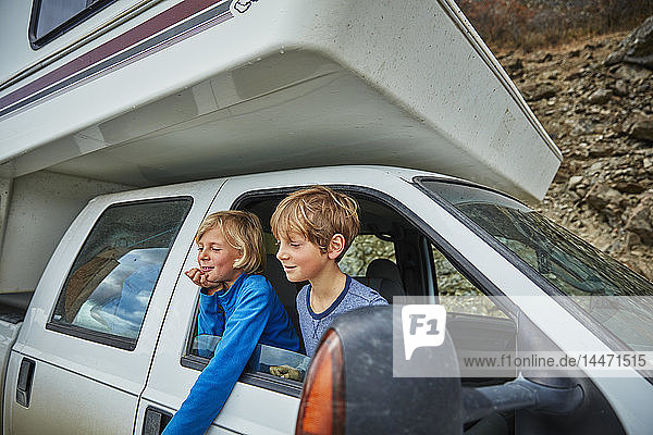 Two smiling boys looking out of window of a camper
