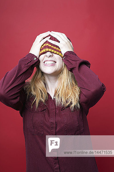 Grinsende junge Frau mit Wollmütze vor rotem Hintergrund