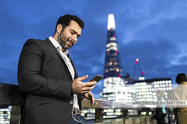 Großbritannien  London  Geschäftsmann unterwegs  der nachts beim Pendeln sein Telefon überprüft