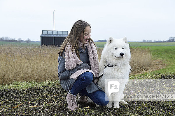 Glückliches Mädchen  das auf einer Wiese neben seinem Hund kauert