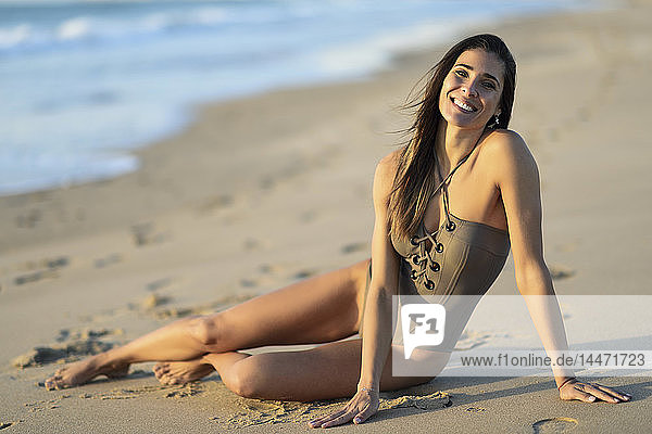 Porträt einer lächelnden schönen Frau im Badeanzug am Strand sitzend