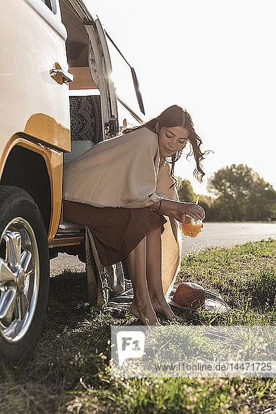 Pretty woman on a road trip with her camper  taking a break  drinking juice