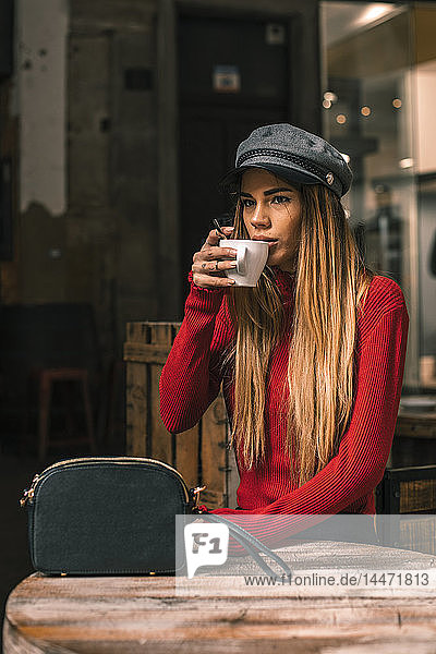 Porträt einer jungen Frau  die auf der Terrasse eines Cafés sitzt und Kaffee trinkt