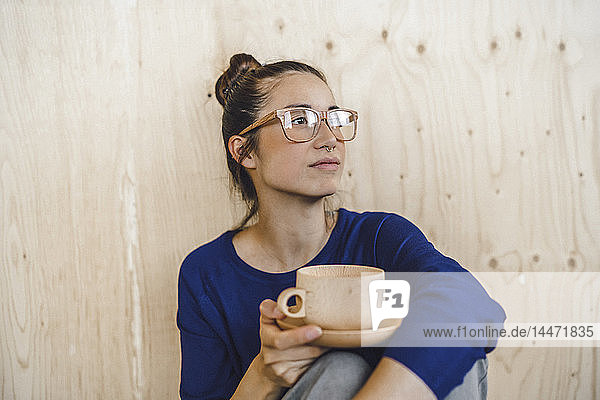 Junge Frau macht eine Pause im Büro und trinkt Kaffee aus einer Holztasse