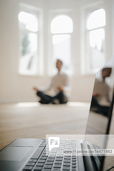 Geschäftsmann in frisch renoviertem Haus  im Schneidersitz auf dem Boden sitzend  meditierend  mit Laptop im Vordergrund