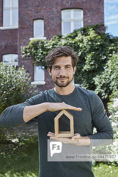 Portrait of confident man in front of his home holding house model