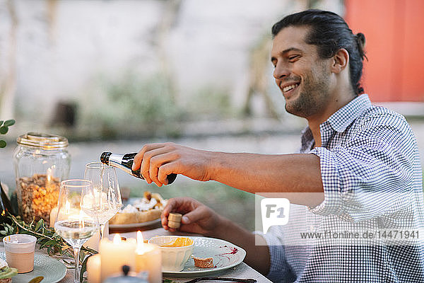 Man pouring out sparkling wine at garden table