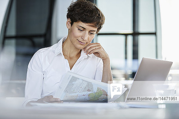 Geschäftsfrau sitzt am Schreibtisch im Büro mit Laptop und Dokument