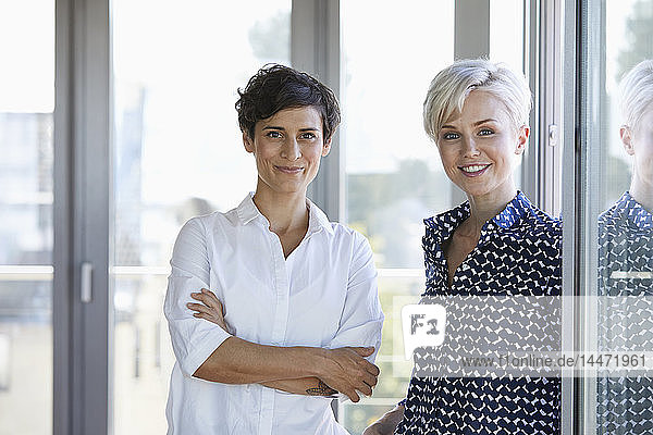 Porträt von zwei lächelnden Geschäftsfrauen am Fenster im Büro