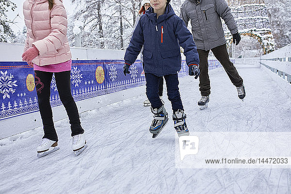Familie mit zwei Kindern beim Schlittschuhlaufen auf der Eisbahn