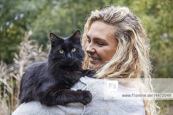 Porträt einer schwarzen Katze auf der Schulter einer lächelnden jungen Frau