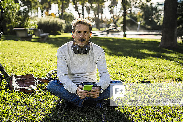 casual businessman sitting on grass in a park  using smartphone