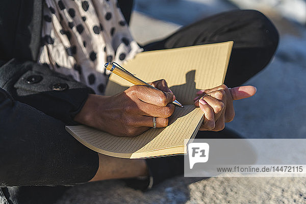 Frau sitzt auf einer Wand und schreibt in einem Notizbuch  Nahaufnahme