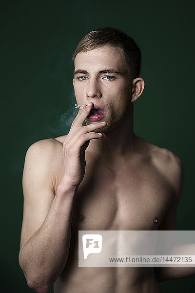 Porträt eines selbstbewussten nackten jungen Mannes  der im Studio eine Zigarette raucht