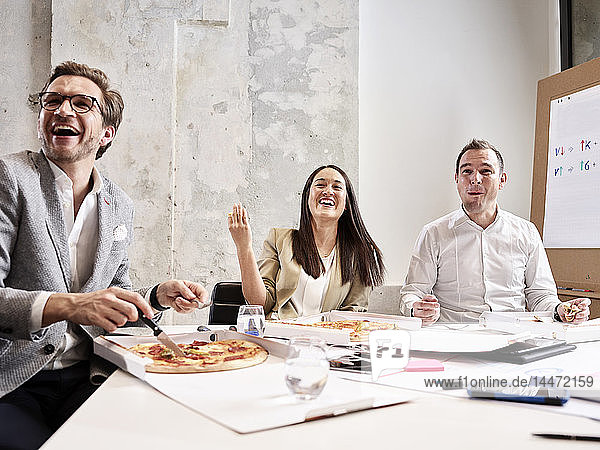 Lachende Kollegen machen Mittagspause mit Pizza im Konferenzraum