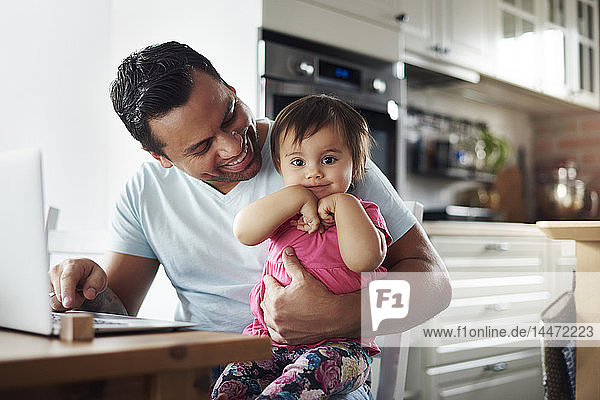 Smiling father with baby girl using laptop on table at home