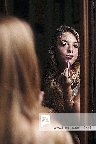 Mirror image of young woman applying lipstick