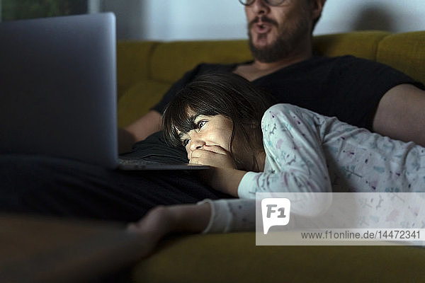 Happy daughter and father looking at laptop on couch at night
