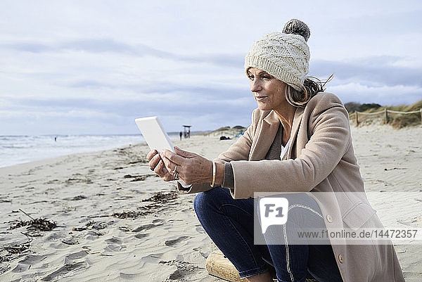 Spain  Menorca  senior woman reading E-Book on the beach in winter