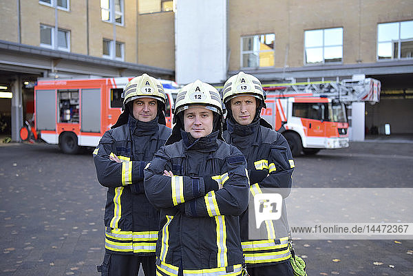 Portrait of three confident firefighters standing on yard in front of fire engine