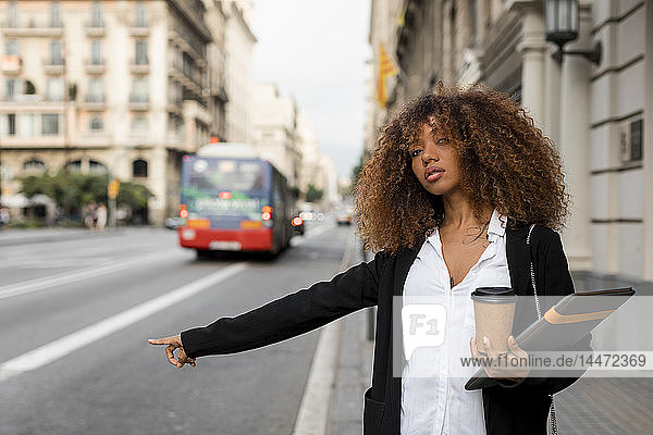 Junge Frau mit Laptoptasche und Kaffee zum Mitnehmen in der Stadt  ein Taxi rufend