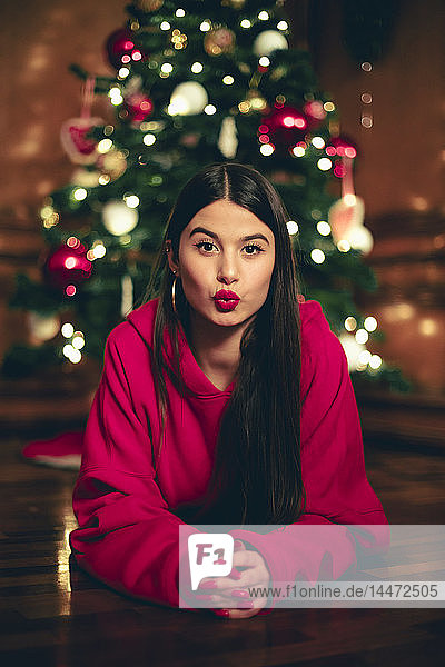 Porträt eines Mädchens  das vor einem Weihnachtsbaum auf dem Boden liegt und schmollt