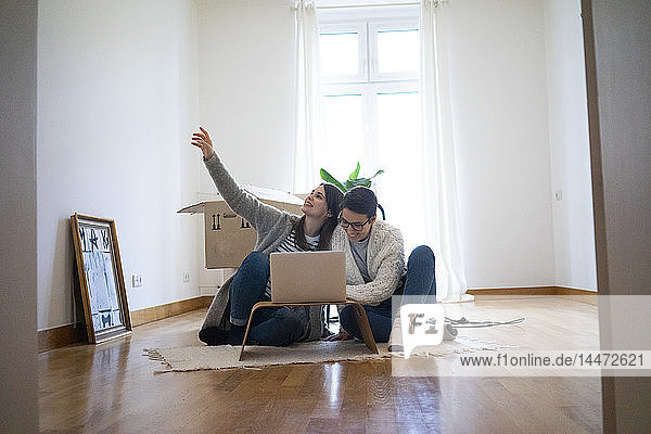 Junge Frauen sitzen auf dem Boden ihrer neuen Wohnung und benutzen einen Laptop