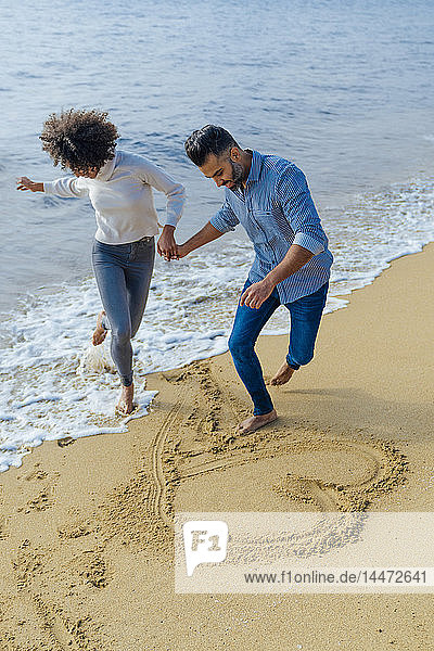 Spanien  Barcelona  glückliches Paar am Strand  das sich am Strand vergnügt und ein Herz in den Sand zeichnet
