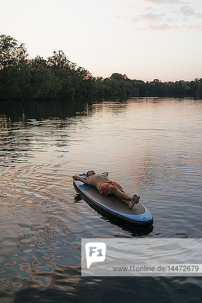 Mann liegt auf einem SUP-Brett auf einem See bei Sonnenuntergang