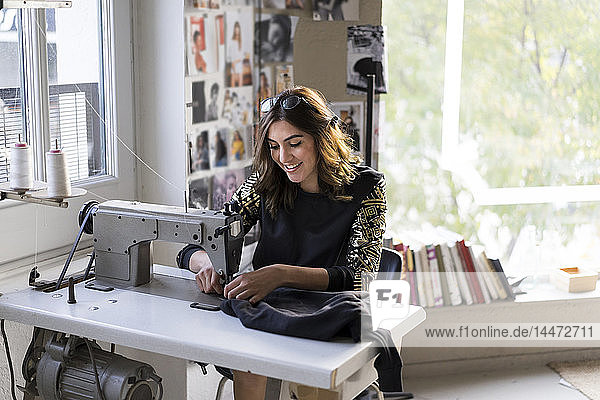Lächelnde junge Modedesignerin mit Nähmaschine in ihrem Atelier