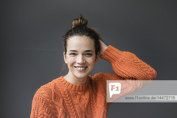 Porträt einer glücklichen Frau in einem orangefarbenen Strickpullover vor grauem Hintergrund
