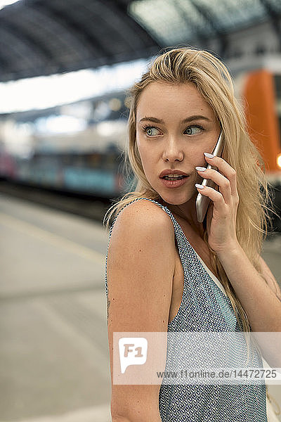 Porträt einer jungen Frau am Bahnhof  die sich am Handy umsieht