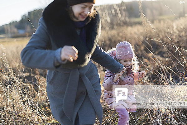 Kleines Mädchen rennt Hand in Hand mit ihrer Mutter zur goldenen Stunde auf der Herbstwiese