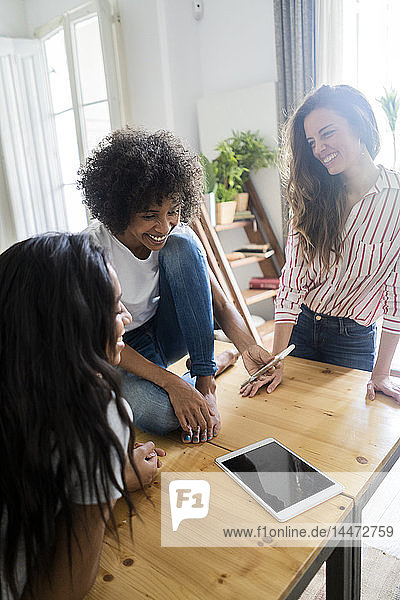 Drei glückliche Frauen schauen auf Handy auf dem Tisch zu Hause