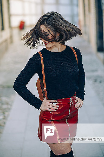Lächelnde junge Frau in rotem Lacklederrock mit Reißverschluss  die ihr Haar wirft