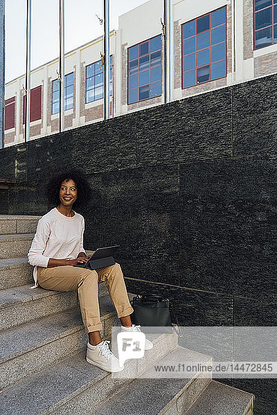Young casual businesswoman using tablet  sitting on steps
