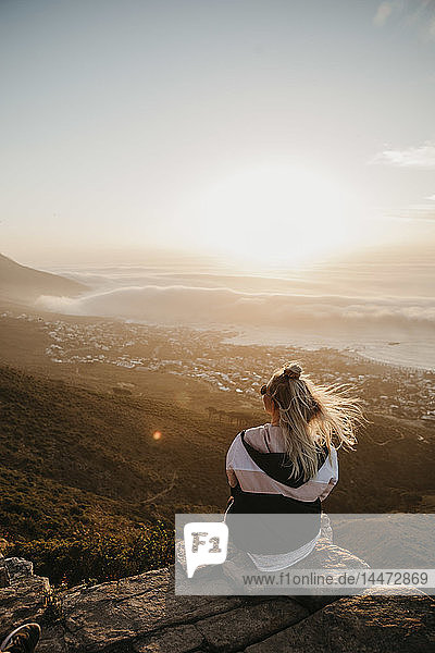 Südafrika  Kapstadt  Kloof Nek  Frau sitzt bei Sonnenuntergang auf einem Felsen