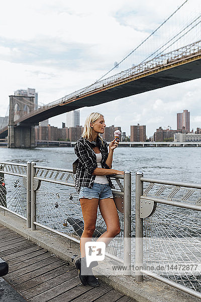 USA  New York City  Brooklyn  young woman standing at the waterfront eating an ice cream