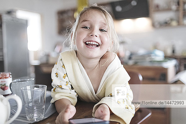 Portrait of happy little girl with smartphone in the kitchen
