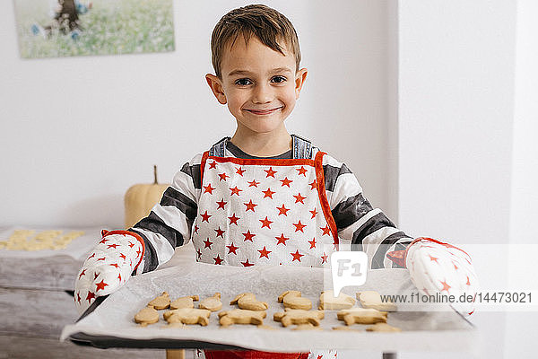 Portrait of smiling little boy holding baking tray with home-made cookies