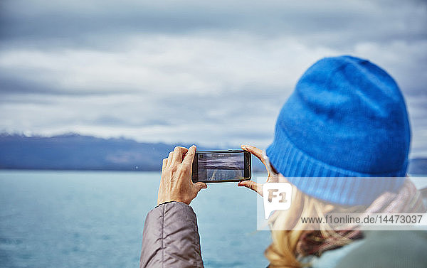 Chile  Puerto Rio Tranquilo  Frau beim Fotografieren von See- und Berglandschaft mit dem Handy