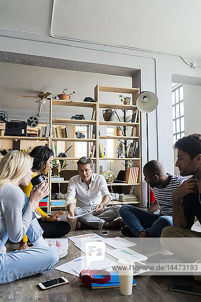 Business team sitting on floor discussing documents in loft office