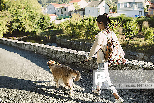 Frau geht mit ihrem Golden-Retriever-Hund auf einer Strasse spazieren