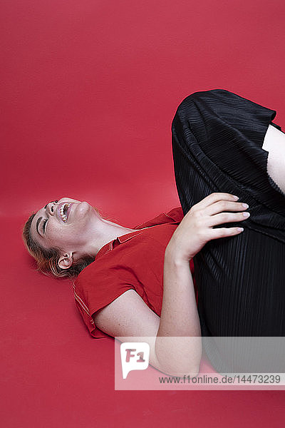 Lachende junge Frau auf rotem Hintergrund liegend