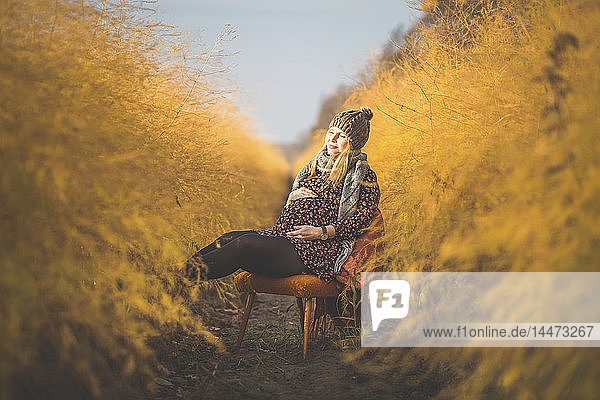 Schwangere Frau sitzt im Herbst auf einem Stuhl im Spargelfeld