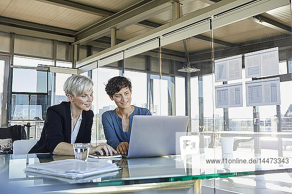 Zwei lächelnde Geschäftsfrauen teilen sich den Laptop am Schreibtisch im Büro