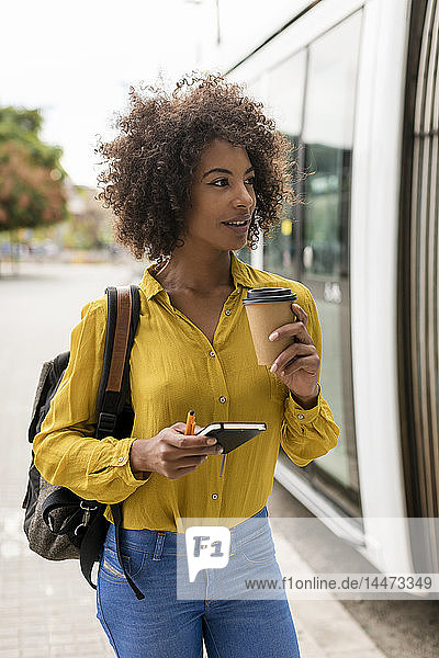 Portrait of smiling woman with coffee to go and notebook in the city